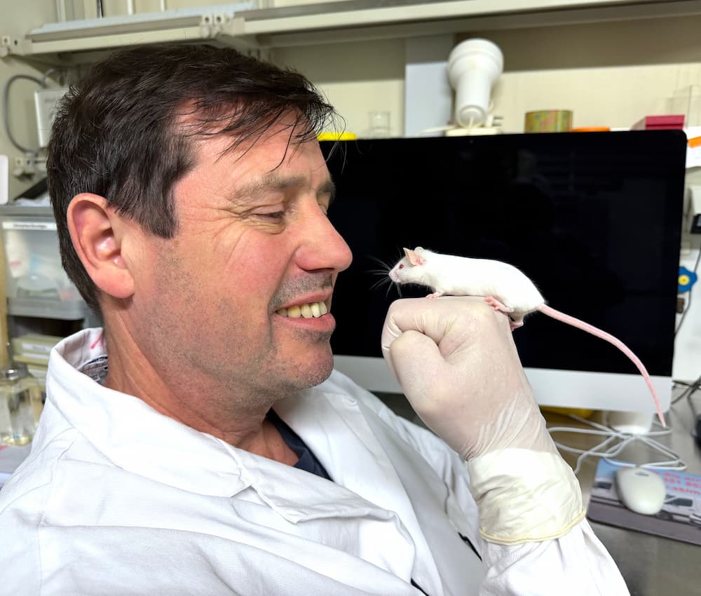 Naumann smiling at a white mouse perched on his hand